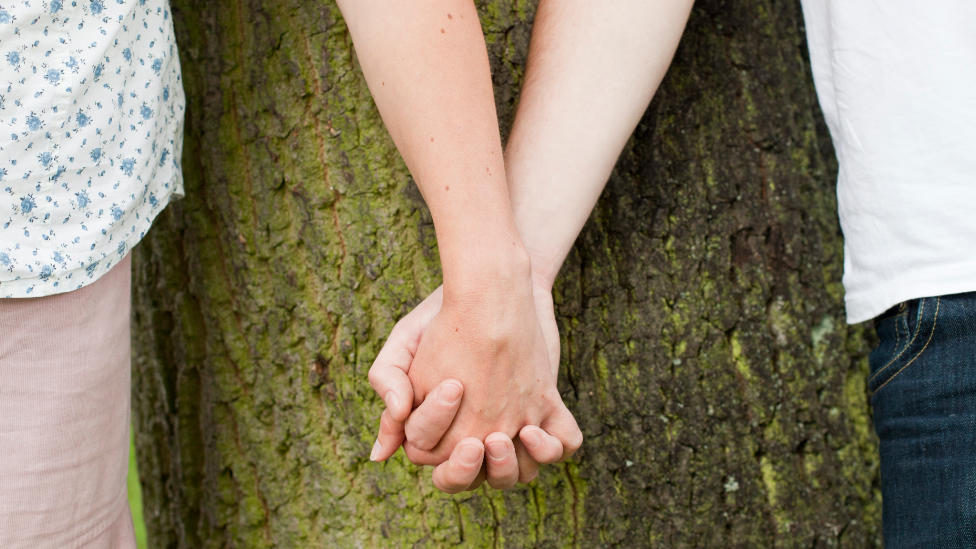 Nahaufnahme: Paar hält Hände vor einem Baum