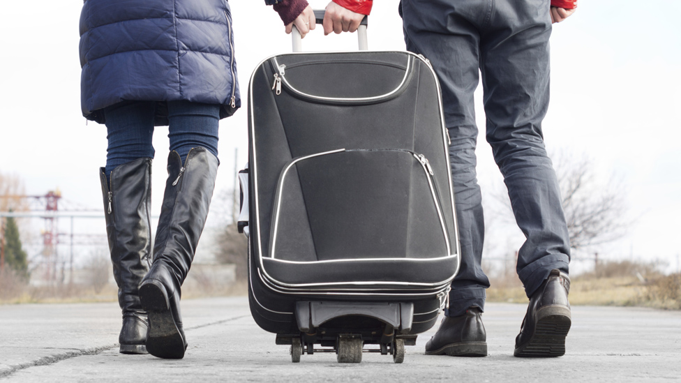 (Quelle: Thinkstock) Ein Paar geht mit einem Koffer die Strasse entlang