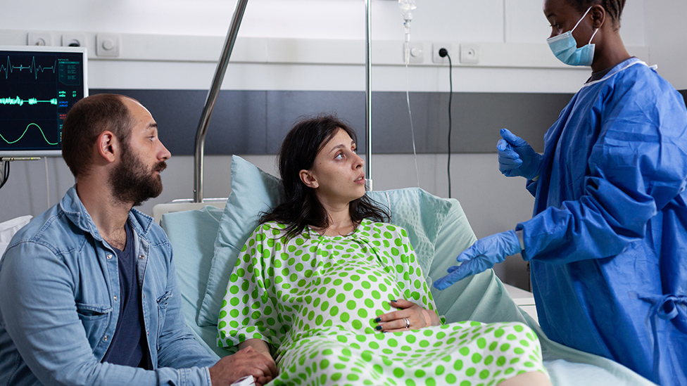 Schwangeres Paar im Krankenhaus, im Gespräch mit medizinischer Fachkraft