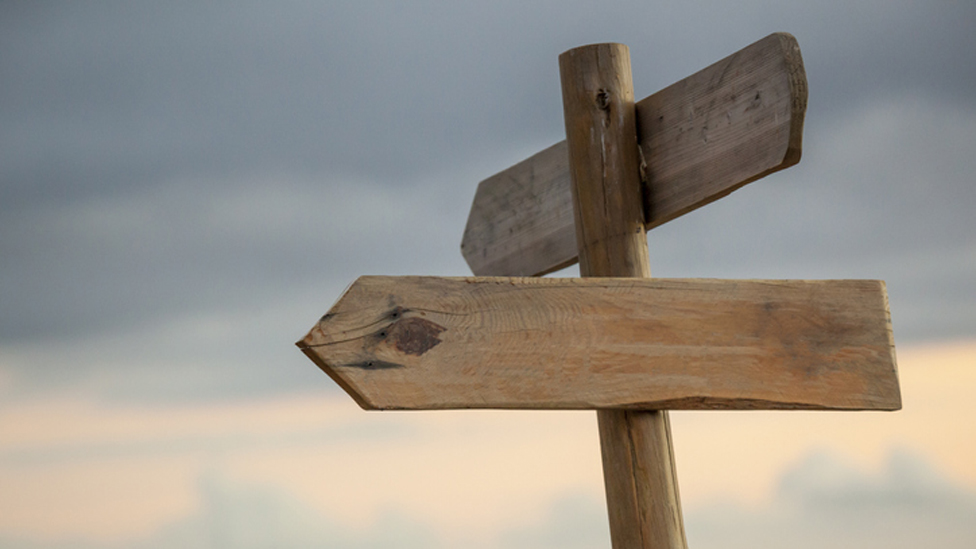 Holzwegweiser Schilder vor gedecktem Wolkenhimmel